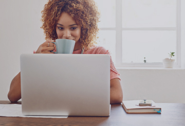 A woman sips from her coffee mug as she looks at her laptop.